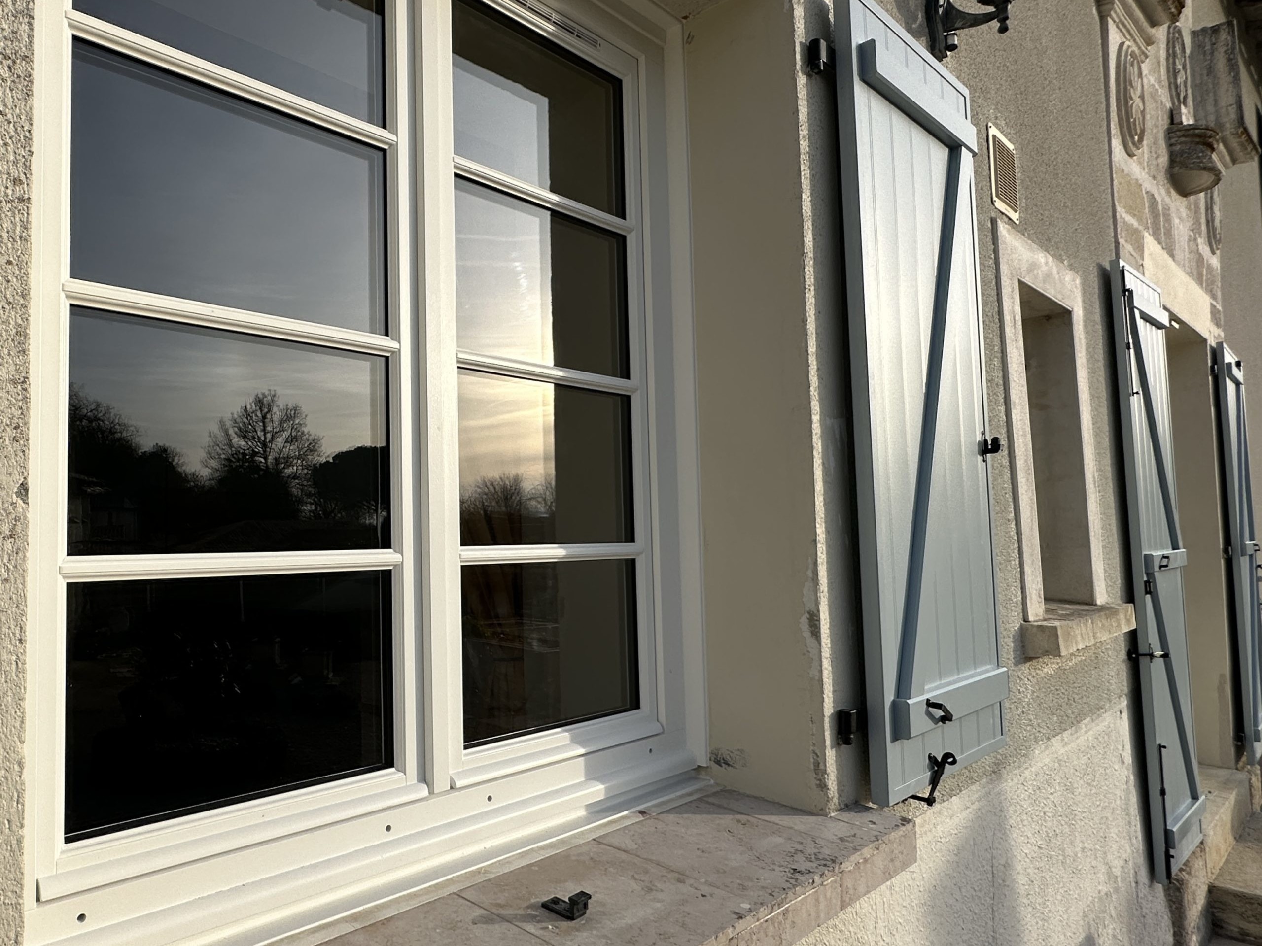 Fenêtres avec volets bleus sur façade ensoleillée.