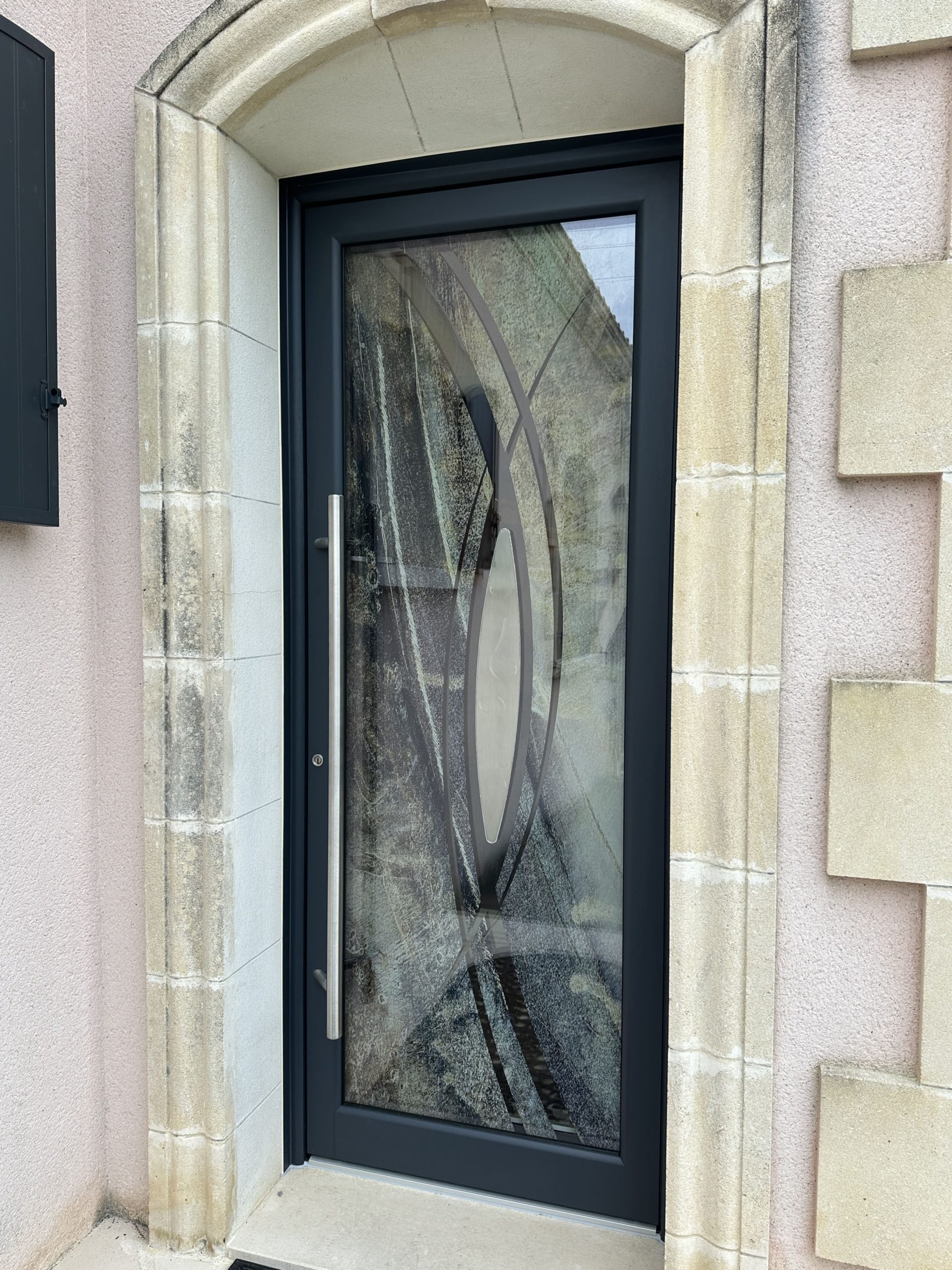 Porte moderne en verre et métal encadrée de pierre.