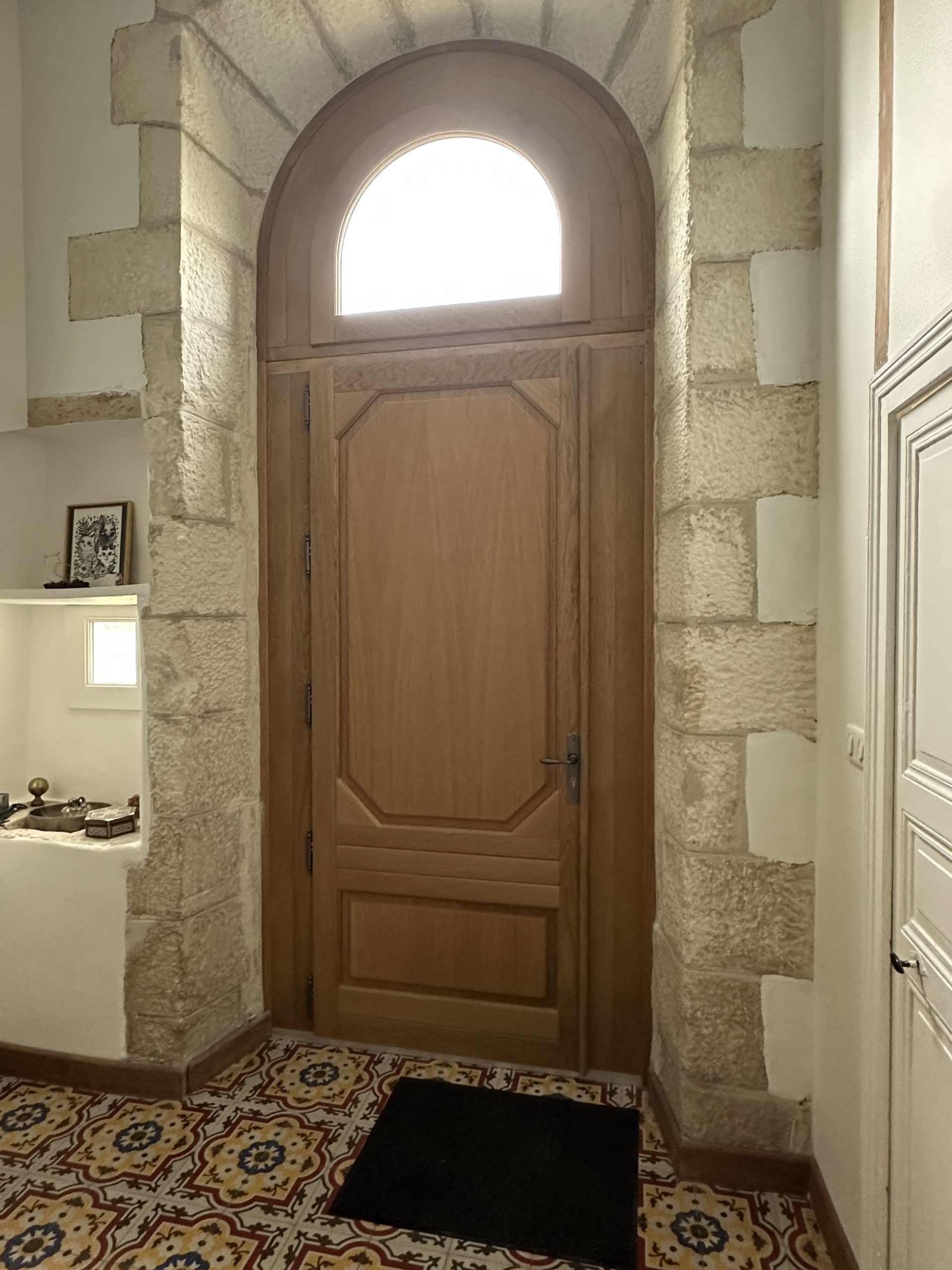Porte en bois avec fenêtre arquée et carreaux colorés.