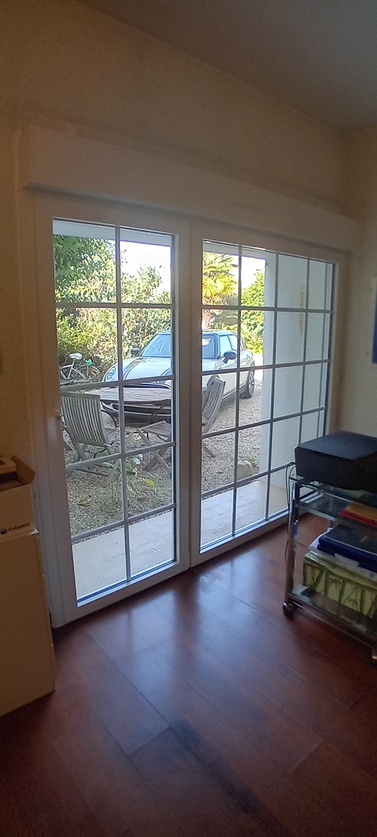 Porte-fenêtre donnant sur jardin avec voiture grise.