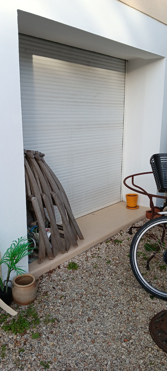 Roulant blanc fermé, vélo, pot et graviers autour.