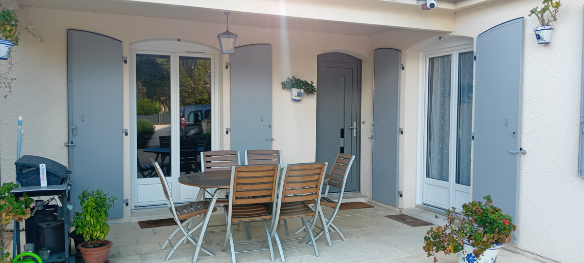Terrasse couverte avec table, chaises et volets gris